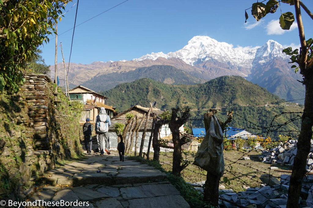 Walking the path out of town.  Fence make of sticks and wire along the walkway.  Mountains in the distance.