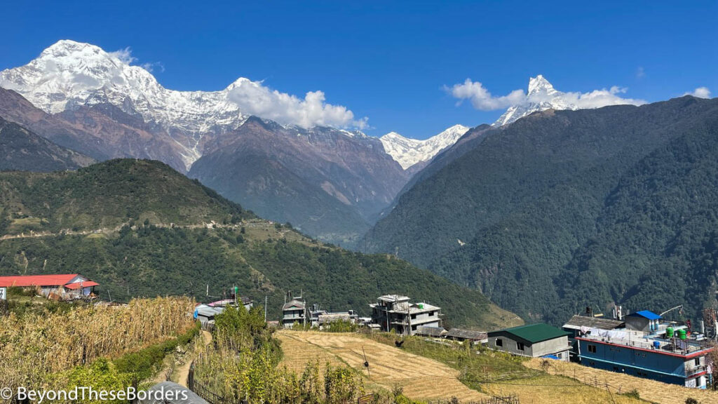 Annapurna range covered in snow behind green and brown mountains beyond the small village.