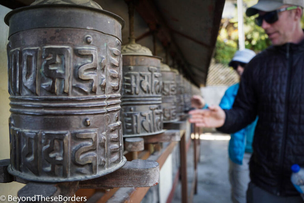 Two hikers spinning metal prayer wheels as they walk around the temple. 