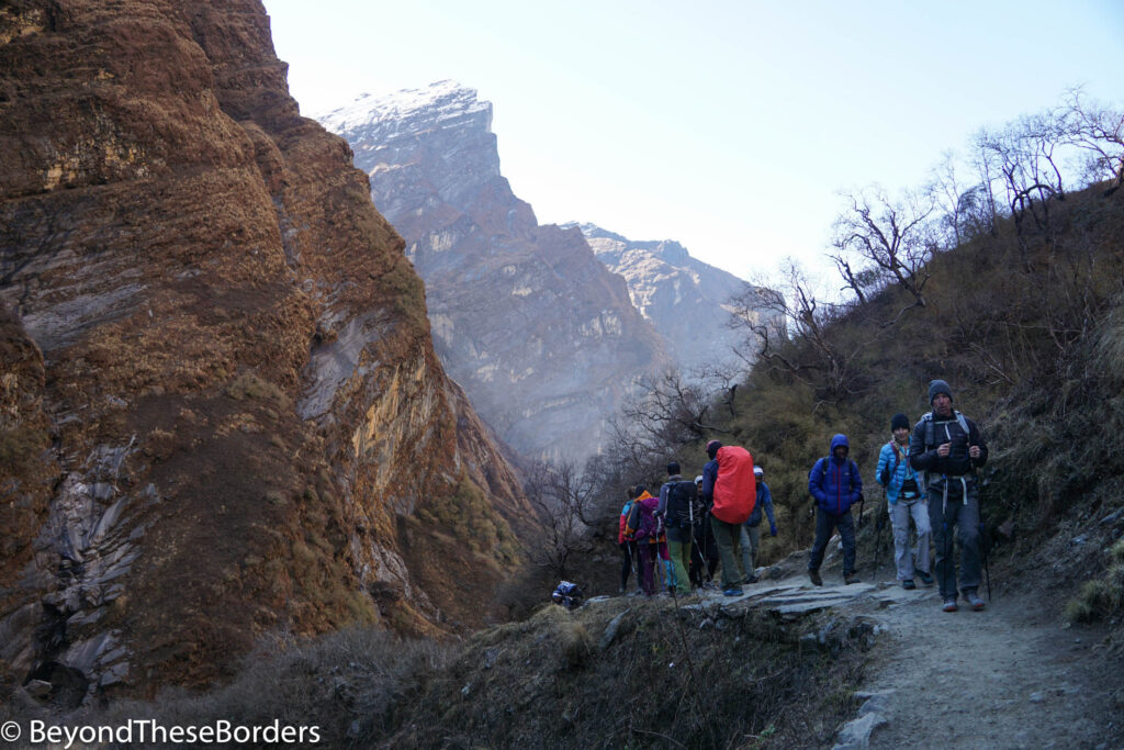 Hikers walking along trail with jagged brown peaks on the other side of the valley.