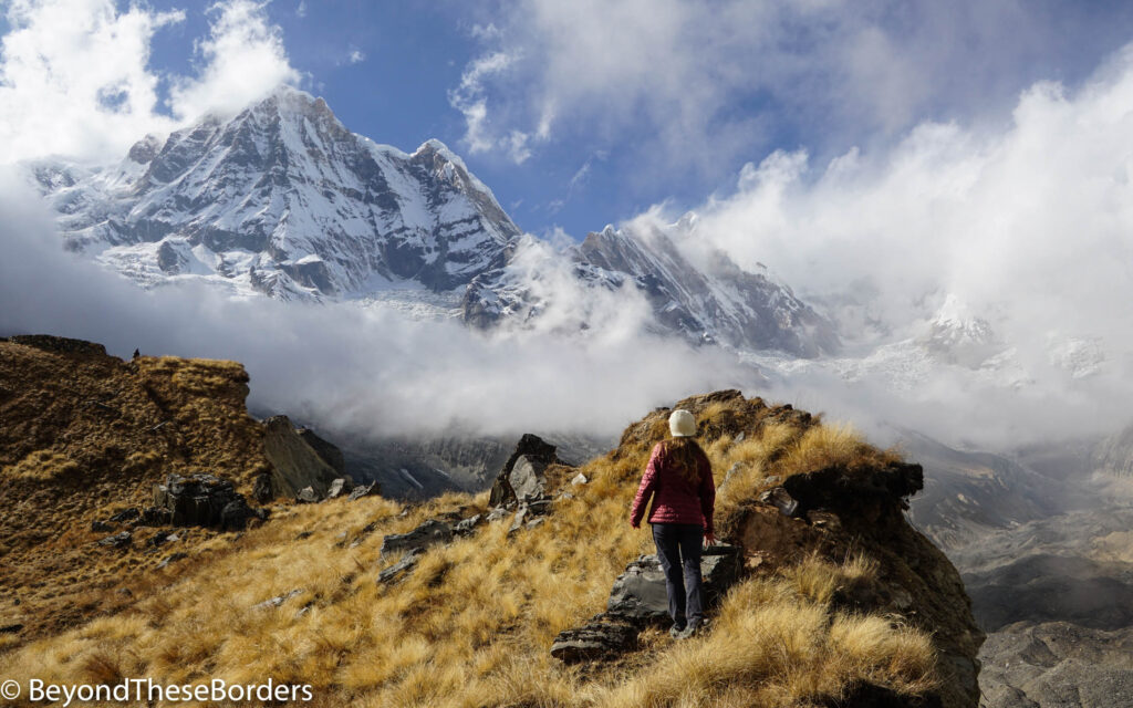 I'm hiking up to a ledge to get a panoramic view of the towering white and grey mountains.  Clouds hovering around the lower third of the closest mountain.