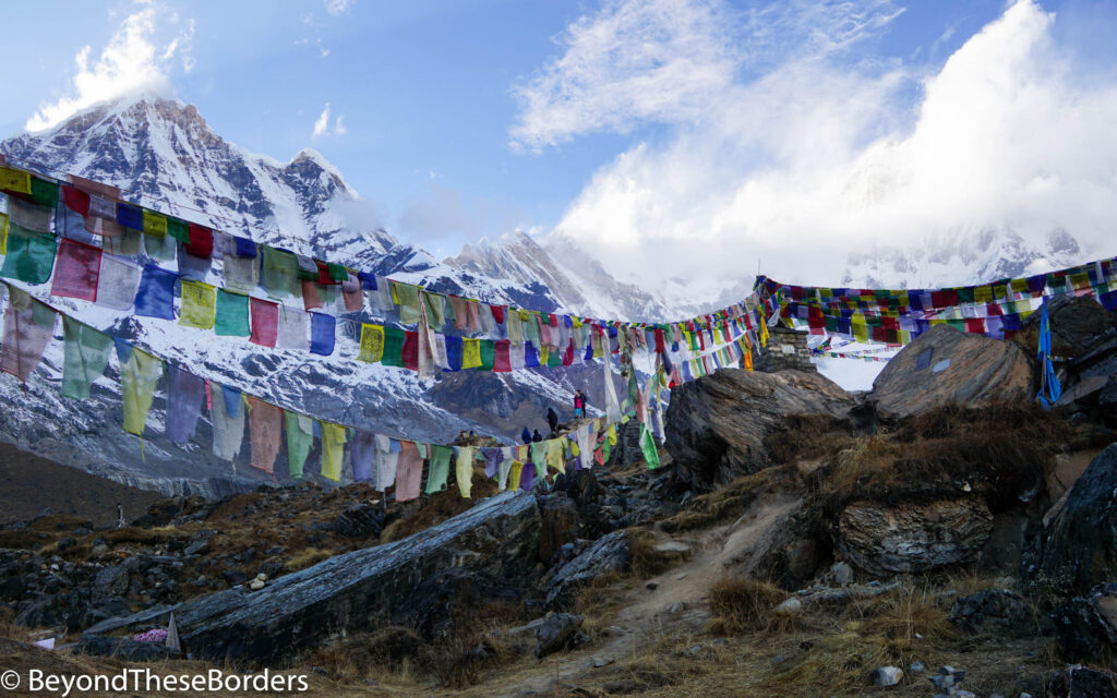 Red, white, blue, yellow, and green prayer flags strung out from a viewing area.  The dramatic mountains creating a panorama behind them.  