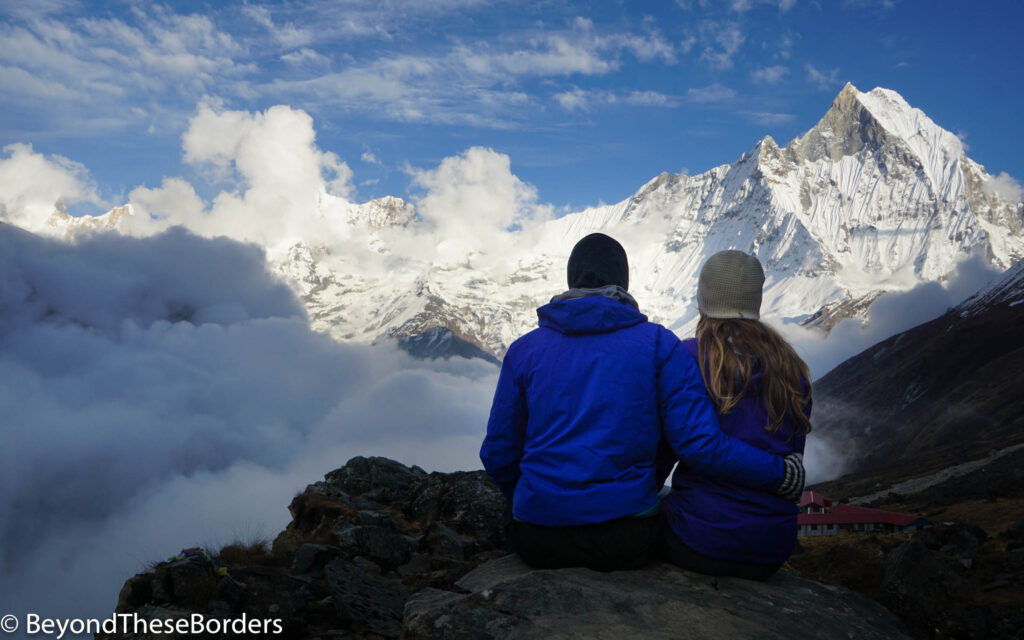 My boyfriend and I sitting, looking out towards the pointed peak of Machhapuchhare mountain.  Thick clouds hand below our altitude in the distance.