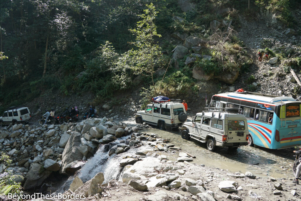Jeeps and a bus stopped in the shallow flowing water of a small waterfall. 