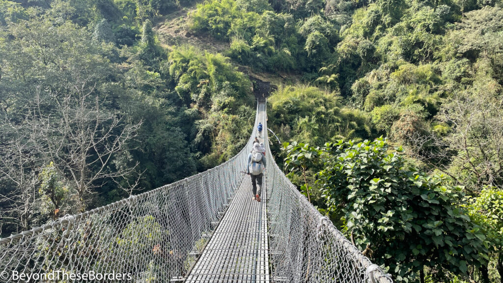 Hikers walking along a long steel bridge towards the green hills on the other side.