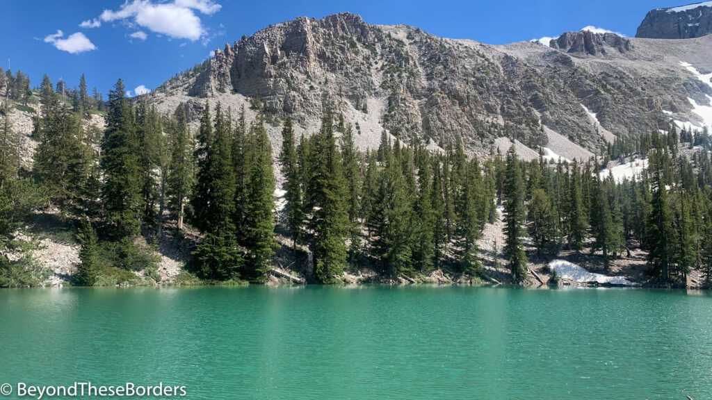 Turquoise water of Teresa Lake with green pine trees surrounding and grey rugged walls of the mountains behind.